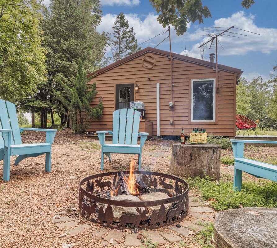 View of the cottage with outdoor seating and fire pit by the water
