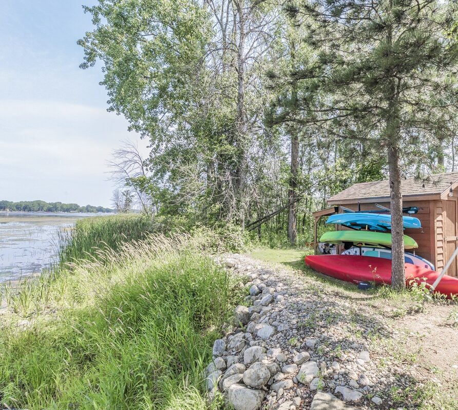 Kayaks, paddleboard, and canoe stored on a rack by the water